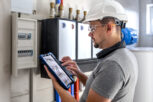Electrical technician looking focused while working in a switchboard with fuses. Man, an electrical technician working in a switchboard with fuses. Installation and connection of electrical equipment. Professional uses a tablet.