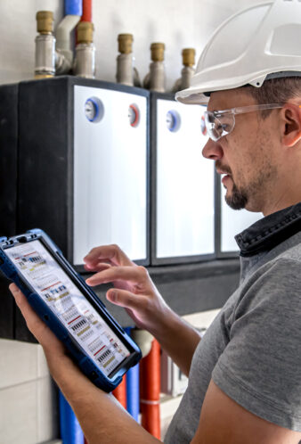 Electrical technician looking focused while working in a switchboard with fuses. Man, an electrical technician working in a switchboard with fuses. Installation and connection of electrical equipment. Professional uses a tablet.