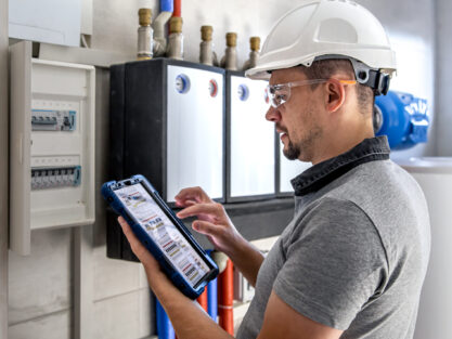 Man, an electrical technician working in a switchboard with fuses. Installation and connection of electrical equipment. Professional uses a tablet.