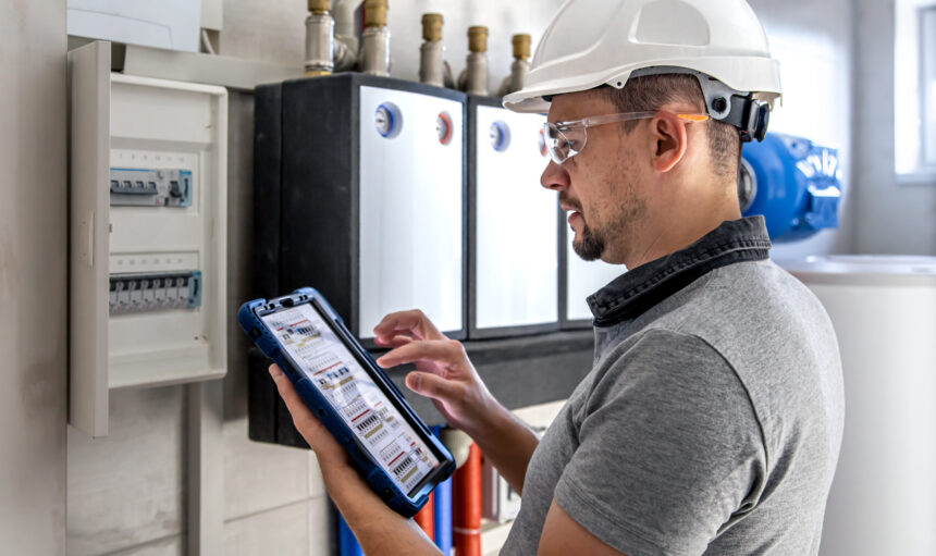 Electrical technician looking focused while working in a switchboard with fuses. Man, an electrical technician working in a switchboard with fuses. Installation and connection of electrical equipment. Professional uses a tablet.