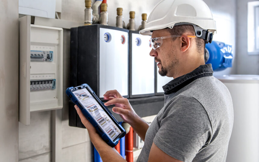 Electrical technician looking focused while working in a switchboard with fuses. Man, an electrical technician working in a switchboard with fuses. Installation and connection of electrical equipment. Professional uses a tablet.